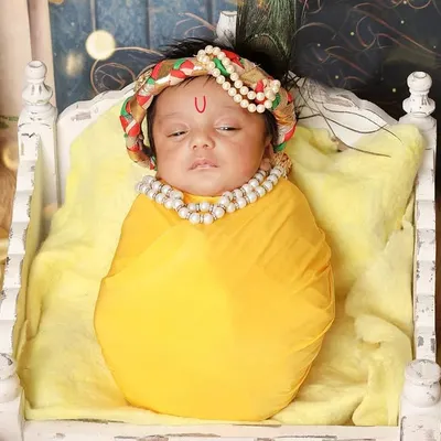My 'Little Krishna' setup captures the divine essence of Janmashtami. Here, a newborn Kanha rests peacefully on a miniature cot, adorned with a pearl necklace and a traditional tilak.