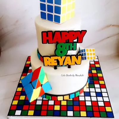 A stunning and complex Rubik's Cube themed cake. This two-tier cake sits on a board that looks like a scrambled cube, and features edible, handcrafted cubes on top.