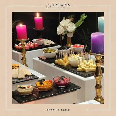 A lavish grazing table set up with an assortment of cheeses, dips, olives, and pita bread, all illuminated by colorful candles for a vibrant presentation.