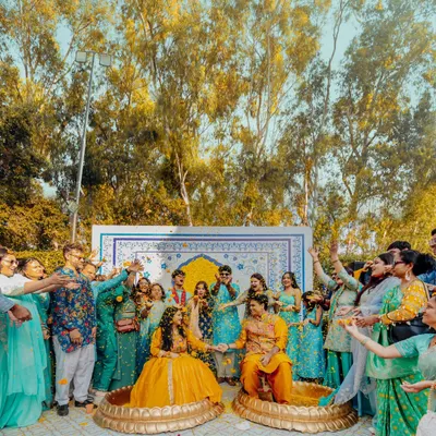 A wide shot of Abhinav and Paromita's Haldi ceremony, surrounded by family and friends. The vibrant yellow and blue decor at Tivoli Bijwasan creates a festive and joyful atmosphere.