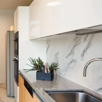 A close-up of this modern kitchen reveals the material palette: glossy white upper cabinets, a durable granite countertop, and a marble-patterned backsplash. These choices balance beauty with resilience, ensuring the space is as practical as it is elegant.
