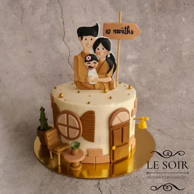 This cake celebrates a family's 10-month milestone with a "Home" theme. The half-kg Vanilla Butterscotch cake features a fondant family figurine on top of their house, with charming details like a tiny cactus and chair.