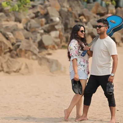 A relaxed and casual pre-wedding photo of a couple walking on the beach. The man carries a guitar, adding a personal touch to this candid moment of them enjoying a day out together.