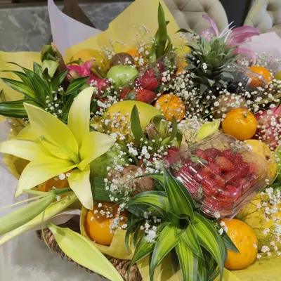 A vibrant and healthy summer fruit hamper. This arrangement features fresh strawberries, mangoes, pineapple, and oranges, beautifully accented with lilies and baby's breath.
