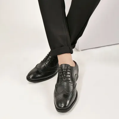 A lifestyle shot of black leather brogues paired with formal trousers. This helps customers see how the shoes look when worn and styled for a specific occasion.
