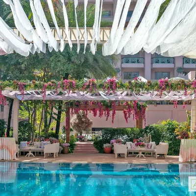 A 'Pomegranate Spring' themed Mehendi party by the pool. The design features elegant pergolas draped in sheer fabrics and bougainvillea, with comfortable lounge seating for a relaxed and celebratory atmosphere.