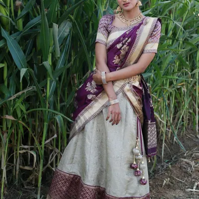 A full-length photo of the purple and cream Langa Voni set against a natural green background. This half saree is a popular rental for photoshoots and traditional events.
