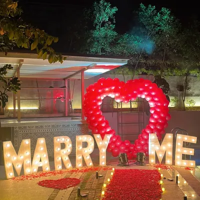The ultimate surprise proposal decoration set up poolside. This features large, illuminated 'MARRY ME' letters, a red carpet runner lined with candles, and a prominent heart-shaped balloon backdrop to guarantee a 'yes'.