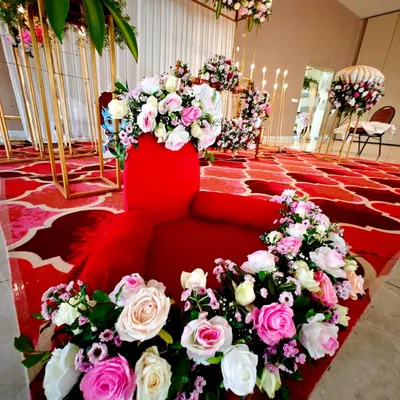 A beautiful setup for a naming ceremony, featuring a red velvet seat adorned with a garland of pink and white roses.
