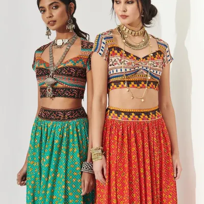A vibrant shot of two models in colorful, mirror-work lehengas, perfect for a Navratri-themed sangeet or Mehendi. The makeup is fresh and glowing, with defined eyes that complement the bohemian-inspired styling.