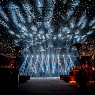 A breathtaking view of a sangeet stage set under a ceiling of thousands of fairy lights, creating a "starry night" effect. The powerful stage lighting and grand scale promise an evening of spectacular performances.