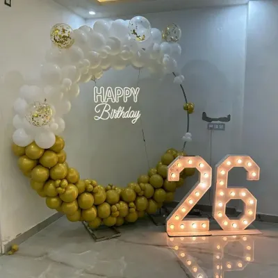 This gold and white theme is pure elegance. The setup features a half-and-half balloon ring, a 'Happy Birthday' neon sign, and large marquee numbers for the 26th birthday, all reflecting beautifully on the glossy floor.