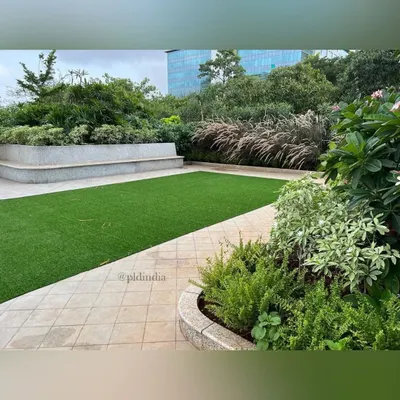 A view of the corporate amenity space, showing the balance between a pristine lawn and lush, mixed-foliage planters. The curved concrete planter with built-in bench seating provides a functional and aesthetic border for the green space.