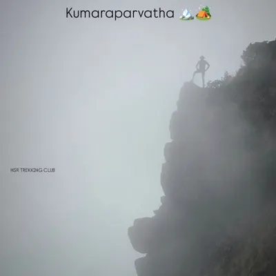 A lone trekker stands silhouetted against the fog on a cliff edge at Kumaraparvatha. This image perfectly captures the moody and epic scale of this challenging trek.