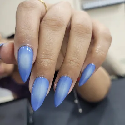 A striking airbrushed ombre effect on long stiletto nails. The vibrant blue fades into a soft white center, creating a bold and futuristic look.