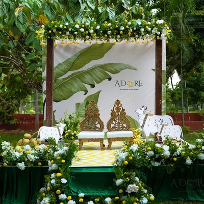 Our 'Banana Grove' theme is a tribute to traditional South Indian aesthetics, perfect for a Varapooje or Muhurtham. The decor features banana leaf motifs, cow cutouts, and intricate carved chairs for the couple.