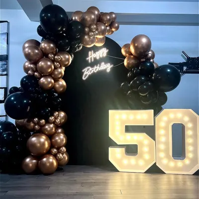 A popular setup for milestone birthdays or corporate anniversaries. This features 4-foot tall marquee numbers, a 'Happy Birthday' neon sign on a matte black backdrop, and a stylish black and bronze organic balloon garland.