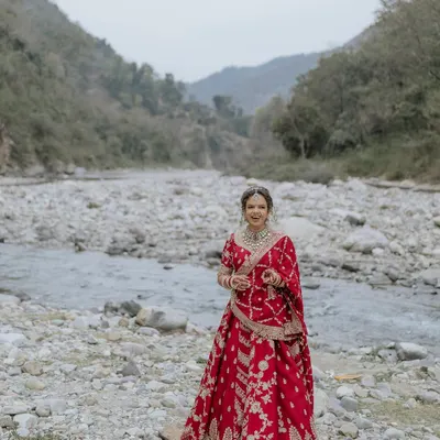 A stunning full-length portrait of the bride in her red lehenga, set against the majestic landscape of Rishikesh.