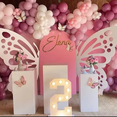 A stunning setup featuring large, white, laser-cut butterfly wings that create a perfect photo opportunity. The pink and lilac balloon arrangement and a light-up marquee number '2' make this an elegant and dreamy second birthday party.