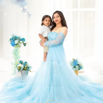 A sweet mother and son portrait. The mother, wearing a beautiful light blue gown, holds her son in a bright, airy studio setting filled with matching blue flowers.