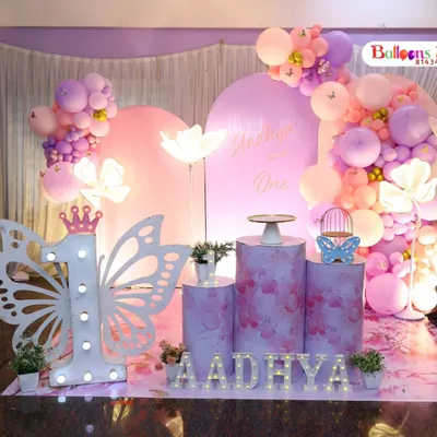 A beautiful butterfly-themed first birthday for Aadhya. This setup includes custom-printed pedestals, large light-up flower props, and a giant illuminated number '1' with butterfly wings.
