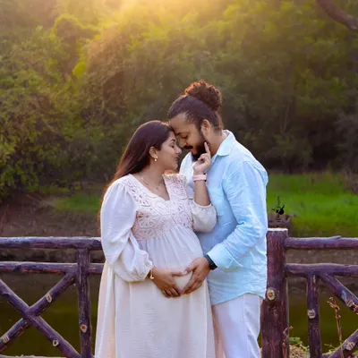 An intimate portrait of an expecting couple, framed by a rustic wooden fence and lush greenery. The warm sunset light adds a romantic glow, perfect for a natural light pregnancy photoshoot.