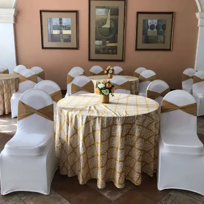 Elegant seating arrangements are crucial for guest comfort and overall aesthetics. Here, we've used round tables with patterned cloths, white chair covers with gold sashes, and simple floral centerpieces for a clean and classic look.