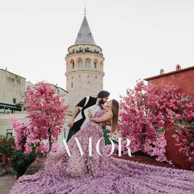 A stunning pre-wedding portrait in front of the Galata Tower in Istanbul, framed by beautiful pink blossoms. This image captures the essence of a romantic, European-style destination shoot.