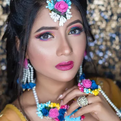 A bold and colorful look perfect for a Mehendi or Haldi function. The vibrant eye makeup, featuring shades of blue and pink, beautifully complements the floral jewelry.