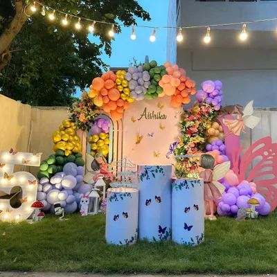 A stunning outdoor garden party with a butterfly theme. This elaborate setup features a massive, multi-colored balloon arch, floral arrangements, large butterfly props, and a light-up marquee number '5'.
