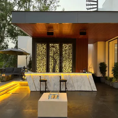 This is a statement bar. It features a geometric marble front, a wooden backdrop with intricate, backlit laser-cut panels, and a fire pit table, creating an incredibly luxurious atmosphere.