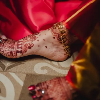 A candid shot of a beautiful henna stain on the foot, adorned with a golden anklet. The design features delicate birds and traditional patterns.