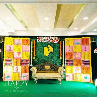 A traditional backdrop for a Seemantham or baby shower ceremony. The design features a colorful grid of fabric panels with marigolds and a central greenery wall.