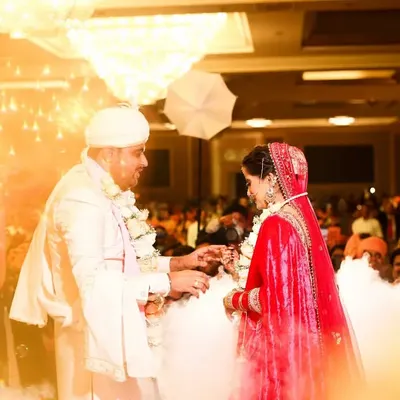 A magical moment during the Varmala ceremony. The couple is surrounded by a dreamy cloud effect and golden light from sparklers, creating an unforgettable, fairytale-like image.