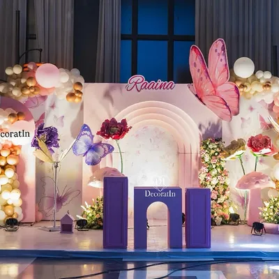 This enchanting stage setup for a butterfly-themed first birthday features a custom arched backdrop, larger-than-life 3D butterflies and flowers, and a beautiful balloon garland. It's the perfect spot for cake cutting and creating lasting memories.