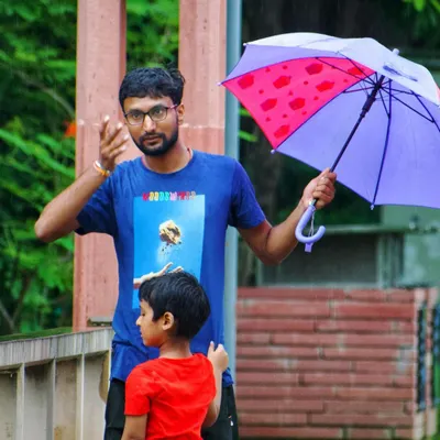 A candid moment between a father and son on a rainy day. The father gestures while holding an umbrella, showing a simple, everyday interaction that is full of narrative.