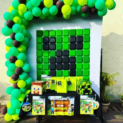 A creative Minecraft themed birthday party setup. The backdrop features a Creeper face made of balloons, with Minecraft-themed gift bags and props ready for the young gamers.
