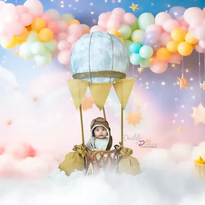A whimsical hot air balloon setup for a sitter session, complete with a pilot cap, fluffy clouds, and a pastel balloon backdrop. This is one of my most requested creative milestone shoots.