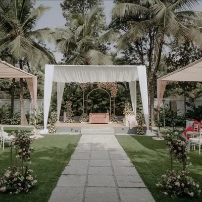 A wide view of an elegant daytime event we designed in a lush garden. The setup features a central stage with a minimalist gold arch, flanked by guest seating under pastel-draped canopies for a soft and romantic feel.