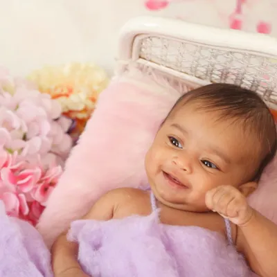 It's always a delight when a baby flashes a happy smile during the session. This candid moment captures a genuine expression of contentment amidst a bed of soft fabrics and flowers.