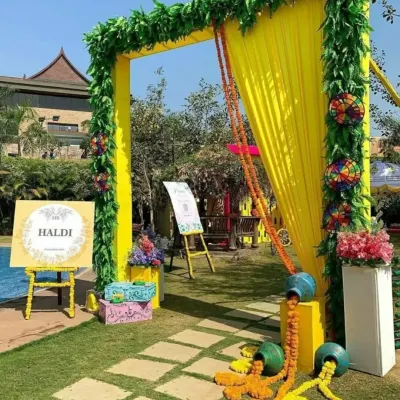 A welcoming entrance for a poolside Haldi event. This setup features a bright yellow arch with green foliage, a personalized "Haldi" welcome sign, and traditional pots with overflowing marigolds.