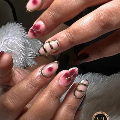 This design is a true work of art, combining multiple techniques. It features a blush pink base with hand-painted wine-red florals, alongside nails with bold, graphic gold chrome lines for a modern, edgy contrast.