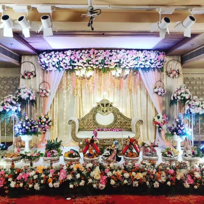 Here is a lavish wedding reception stage I designed. The setup features a beautiful floral canopy with hanging chandeliers over an ornate golden sofa, with a sea of my decorative trays and flower arrangements creating a truly grand display.