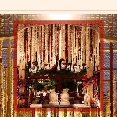 A view of the traditional red and white floral mandap from the side. The structure is covered in strings of tuberose and red carnations, creating a dense, fragrant canopy.