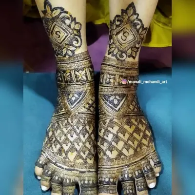 An intricate bridal mehandi design for the feet, featuring a dense net pattern and personalized initial 'S' motifs. The design covers the entire top of the foot and toes.
