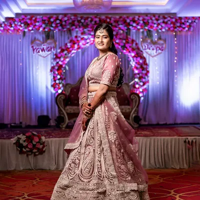 A full-length portrait of the bride, Deepa, showcasing her magnificent lehenga and the grand decor of the wedding venue.