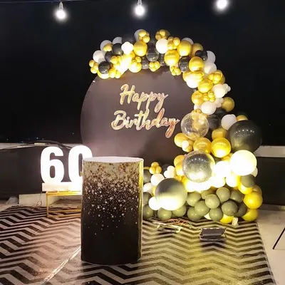 A sophisticated setup for a 60th birthday celebration. The black, gold, and white balloon arch frames a custom circular backdrop, complemented by large light-up numbers for a classy look.