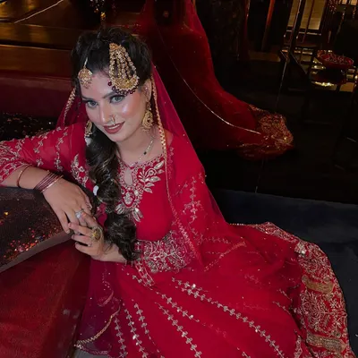 A full-length view of the traditional Pakistani bridal look. The magnificent red anarkali, paired with heavy gold jewelry and a long braid, creates an image of pure regality and grace.