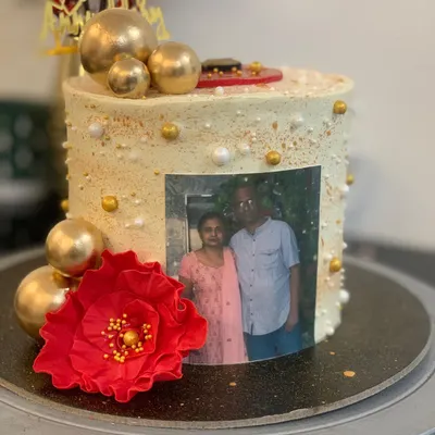 A special silver jubilee cake celebrating 25 years of marriage. It features an edible photo of the couple, a beautiful red sugar flower, and elegant gold details.