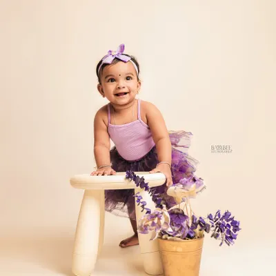 This is a beautiful, classic studio portrait of a one-year-old girl in a lovely purple outfit. The lighting and her sweet smile are perfect on their own.